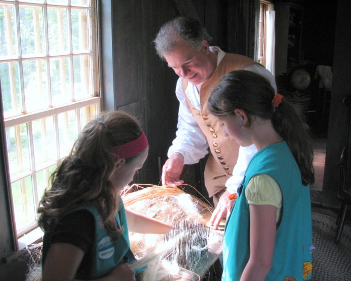 PETER GIAMMARCO demonstrates recently how flax is prepared for spinning as Abigail Goncalves, left, and Elizabeth Lambert help at the Smith-Appleby House in Smithfield. The historic building is one of 29 in the Rhody Ramble program, which has four new members. The program provides exposure to hands-on activities for families. / COURTESY DON GONCALVES