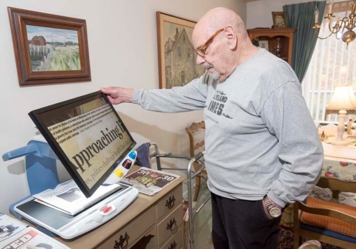 THE BIG PICTURE: Stephen Mitchell uses his video magnifier to read at his condo in Narragansett. Mitchell has macular degeneration and uses the magnifier to read his newspaper, the mail and pill bottle labels. Several nonprofits are experiencing demand for this type of technology and iPads in particular, and the nonprofits that work with the Rhode Island Assistive Technology Access Partnership have experienced staffing growth and increases in demand for these devices in the past year. / PBN PHOTO/MICHAEL SALERNO