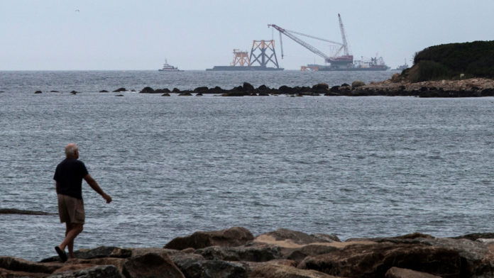 A MAN walks on rocks as a Deepwater Wind LLC offshore wind farm stands under construction off the coast of Block Island on July 27. / BLOOMBERG NEWS FILE PHOTO/SHIHO FUKADA