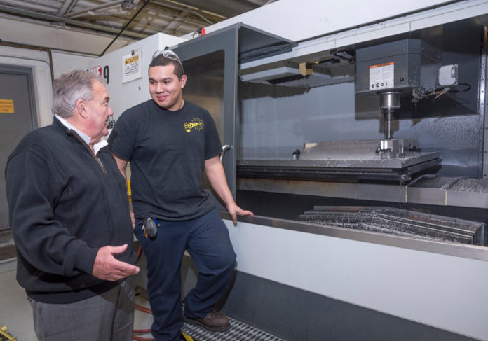 PATH TO SUCCESS: Edward Forero, right, a CNC intern at Hope Valley Industries in North Kingstown, speaks with the owner of the company, Tom Melucci. Hope Valley Industries manufactures and distributes automotive accessories, such as floor mats. The company has strategically embarked on training and apprenticeship programs. / PBN FILE PHOTO/MICHAEL SALERNO