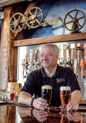 PINT-SIZED: Ron Koller, owner of The Malted Barley in Providence, holds pints of craft ales Arrogant Bastard, left, by Stone Brewing Co. of California, and Brooklyn Larger, by Brooklyn Brewing Co. of New York. / PBN PHOTO/MICHAEL SALERNO