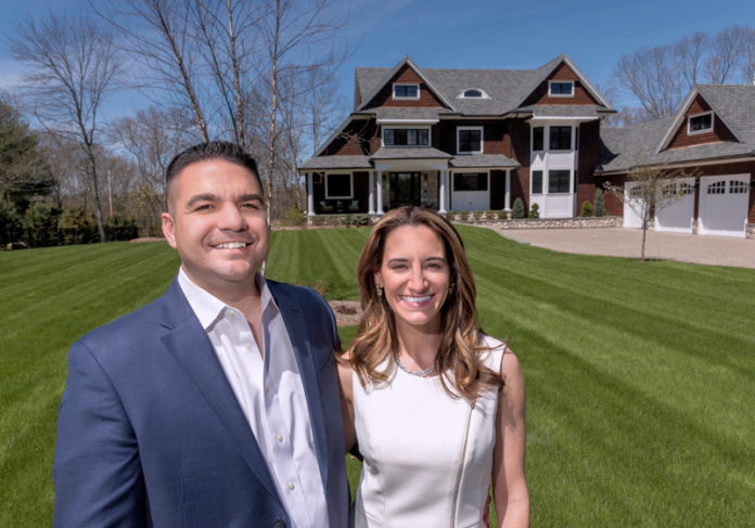 FORM AND FUNCTION: Jennifer and Gary Mello, owners of Seekonk-based The Mello Group, are seen in front of a home that Gary Mello designed. The 4,000-square-foot home has a large, open living area, a 12-foot island in the kitchen and a two-sided, two-story chimney with a fireplace both inside and out. / PBN PHOTO/MICHAEL SALERNO