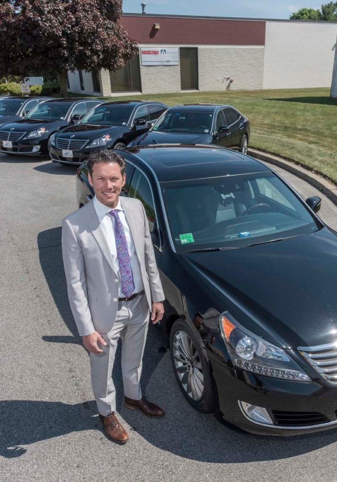 SAFETY FIRST: John Olinger, president and CEO of All Occasion Transportation, is seen with some of the cars in his fleet of vehicles. Olinger believes transportation network companies should be subject to regulation, citing their opposition to background checks on their drivers as a public-safety issue. / PBN PHOTO/MICHAEL SALERNO