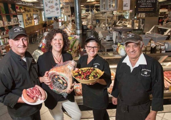 TASTE oF ITALY: From left, John Pasquale, manager of Venda Ravioli, holding a plate of Tuscan-style sausage and frenched beef short ribs, Savoring Rhode Island owner Cindy Salvato, holding prosciutto, a cured Italian ham, Candice Duran, holding imported Cerignola olives, and Aldo Ricci, meat processor, are seen in the popular Federal Hill Italian grocery store and eatery. / PBN PHOTO/MICHAEL SALERNO