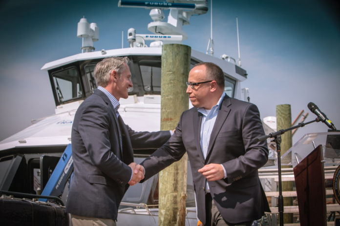 NEW COURSE: At Quonset Point in North Kingstown, Charles A. Donadio Jr., president of Rhode Island Fast Ferry, left, shakes hands with Jeffrey Grybowski, CEO of Deepwater Wind LLC, at the April christening ceremony for the United States' first offshore-wind service vessel, The Atlantic Pioneer, in which Donadio invested $4 million. / COURTESY TRIPP BURMAN PHOTOGRAPHY