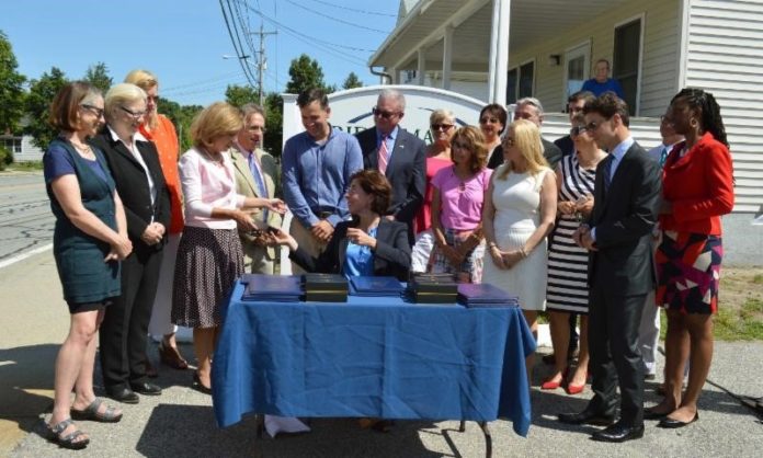 GOV. GINA M. Raimondo, seated, gives Senate President M. Teresa Paiva Weed a pen as other legislators, advocates and individuals in recovery look on. Raimondo signed eight bills into law aimed to help curb the opioid crisis at a ceremony Tuesday at Bridgemark Addiction Recovery Services. / COURTESY GOVERNOR'S OFFICE