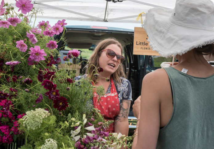 BLOOMING BUSINESS: Anna Jane Kocon, left, owner and founder of the Little State Flower Co., at the Aquidneck Growers' Market at Newport Vineyard & Winery. She sells a variety of cut flowers there on Saturdays. / PBN PHOTO/MICHAEL SALERNO