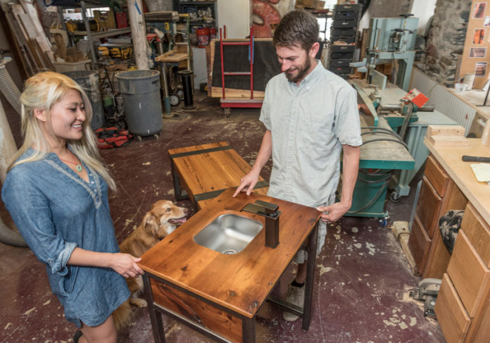 REFINED RECYCLING: Christian T. Descoteaux, right, and Huetran Duong run Christian Thomas Designs LLC. Shown are a vanity made from reclaimed fir and polished steel and a table of reclaimed hard pine beams wrapped in hollow steel. / PBN PHOTO/MICHAEL SALERNO