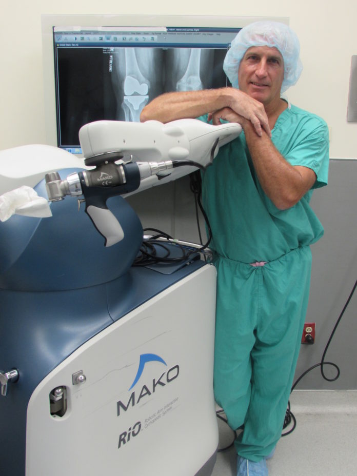 DR. BOB MARCHAND stands in a South County Hospital operating room with Mako equipment, which is used to assist in hip replacements, and partial and full knee replacements. / COURTESY SOUTH COUNTY HOSPITAL