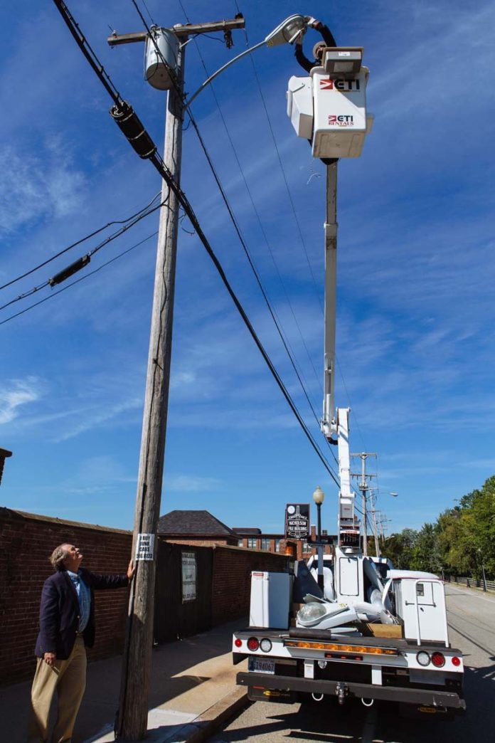 TALL ORDER: The Partnership for Rhode Island Streetlight Management, founded and led by Jeffrey A. Broadhead, left, is helping cities and towns find significant savings by converting streetlights to light-emitting diodes. Installing a new light in Providence is electrician Jim Mitchell.