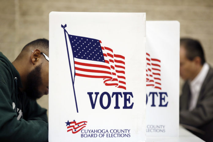 VOTERS CAST ballots at the St. Thomas More polling location in Cleveland on Nov. 8. The Justice Department will deploy 500 personnel to polling stations, including those in Providence and Pawtucket, on Election Day to help protect voters against discrimination and intimidation. / BLOOMBERG NEWS PHOTO/LUKE SHARRETT