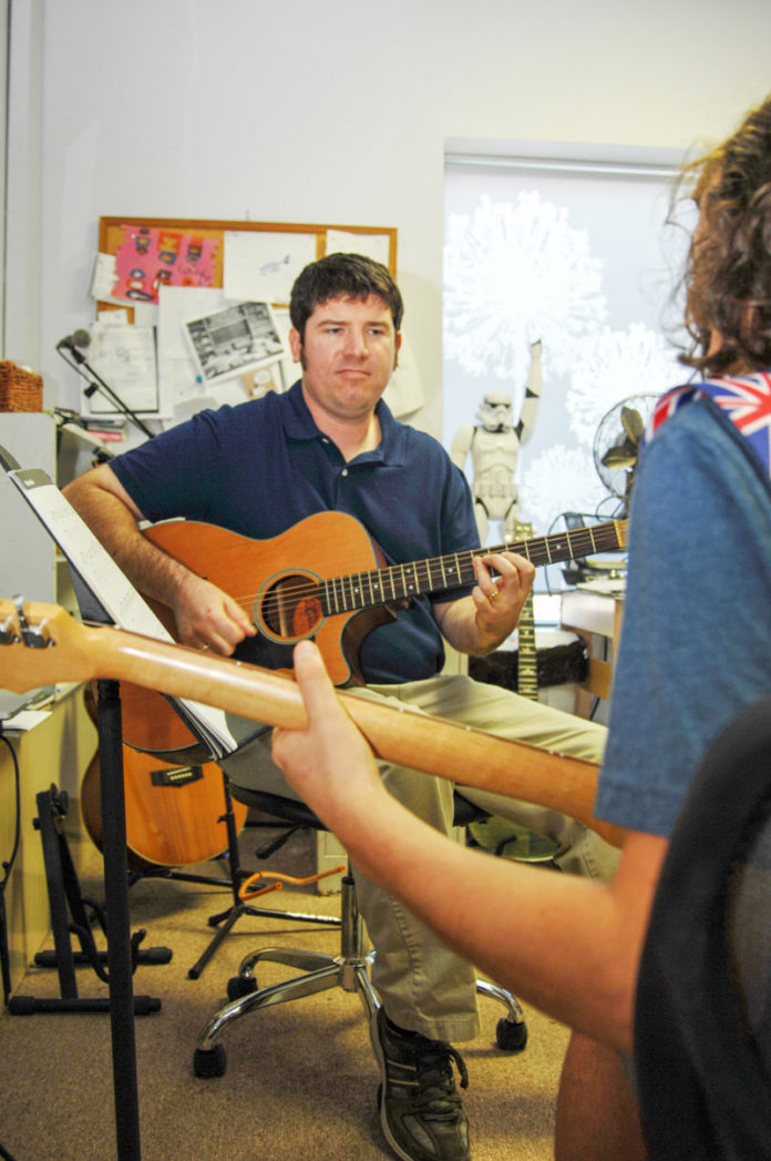 STRIKING A CHORD: The Band Room owner Tom Foley gives student Justin Holland a guitar lesson in the Westerly music shop. / PBN PHOTO/BRIAN MACDONALD