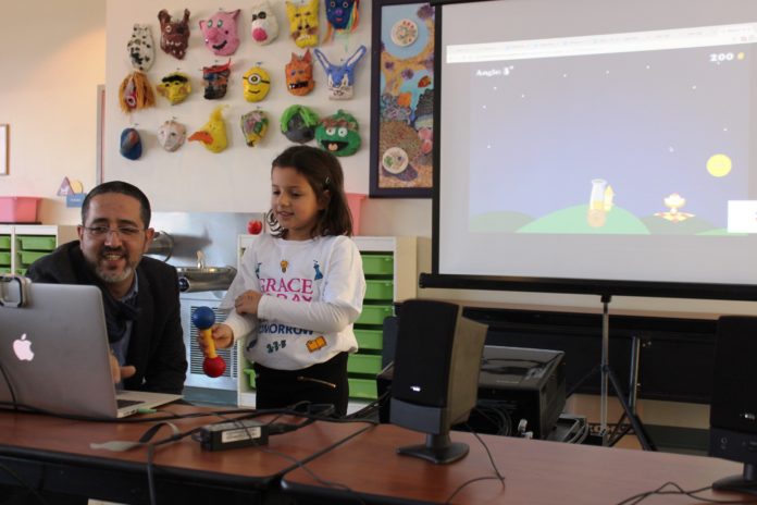 TIMOCCO INC. CEO Eran Arden shows Mia Izzi Pirotto how to use the company’s latest therapeutic gaming technology that allows users to practice more complex hand and wrist movements while playing games online. The game used motion-based technology to track the movements for children with special needs. Timocco has been testing the game with students and staff at Providence’s Meeting Street school as well as with faculty from Brown University and Hasbro Children’s Hospital. / COURTESY TIMOCCO INC.