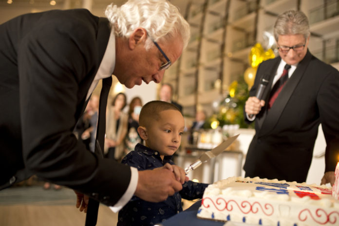 LEN IANNUCCILLI, owner of RE/MAX Professionals in East Greenwich with his brother David (holding the microphone), helps Kyrie White, the Hasbro Children’s Hospital 2016 CMNH Champion, cut the cake at a fundraising gala in celebration of the 30th anniversary of RE/MAX in Rhode Island. / COURTESY RE/MAX IN RHODE ISLAND