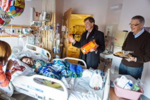 ANNUAL TRADITION: Former Hasbro CEOs Alan G. Hassenfeld, center, and Al Verrecchia, right, visit Ryan Hebert, 7, and his mother, Jeanne Hebert, at Hasbro Children's Hospital. Each year, the duo visits the hospital to hand out gifts to children and visit with parents. / PBN PHOTO/RUPERT WHITELEY