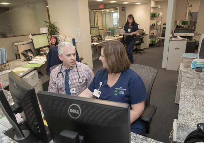 HIDDEN GEM: Gerald A. Colvin, director of the new cancer center in South County Hospital, discusses a patient's case with Lisa Willis, medical receptionist. In the background is Dawn White, medical receptionist. / PBN PHOTO/MICHAEL SALERNO