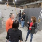 PARTNERING FOR THE LONG RUN: The Beck Companies looks to create long-term customer relationships across its business lines. Here, Tracey Beck, co-owner, right, meets with customers Jo Polis, left, and Annalyn Bauer, back to camera, from Lebanon, Conn., while in the background employees Jon Mitchell, left, and Eric Backstrom move stone slabs at the company's North Smithfield facility. / PBN PHOTO/MICHAEL SALERNO