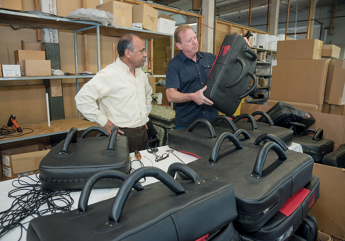 EXPANDING STRENGTHS: John Caito III, right, president of Desmark Industries and its new division, Amerisewn, which designs, engineers and manufactures complex stitched products, speaks with stitcher Alejandro Batz about the body shields they are manufacturing. / PBN PHOTO/MICHAEL SALERNO