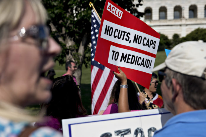 A DEMONSTRATOR OPPOSED to the Senate Republican health-care holds a sign that reads 