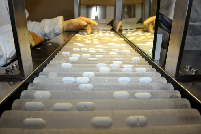 AN EMPLOYEE USES a machine that sorts pills. / BLOOMBERG FILE PHOTO/ANTOINE ANITONIOL