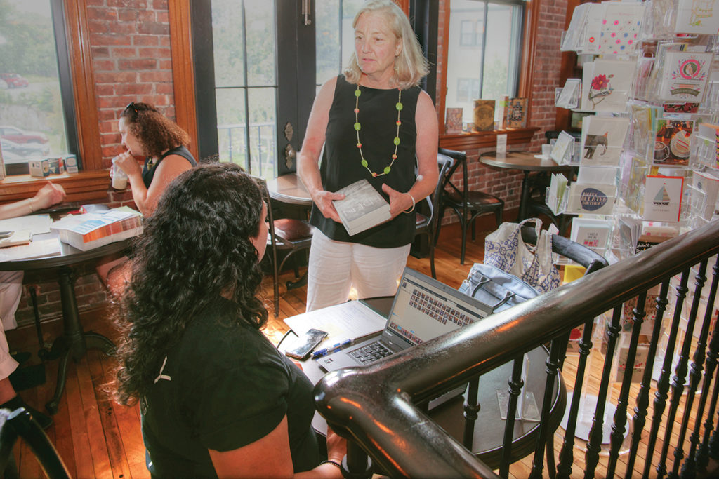 BOOSTED PROFILE: Annie Philbrick, standing, owner of Savoy Bookshop & Café in Westerly, visits with customers enjoying the café. Philbrick says the shop benefited from increased sales after a photo of former first lady and Democratic presidential candidate Hillary Clinton shopping there went viral following the 2016 presidential election. / PBN PHOTO/BRIAN MCDONALD