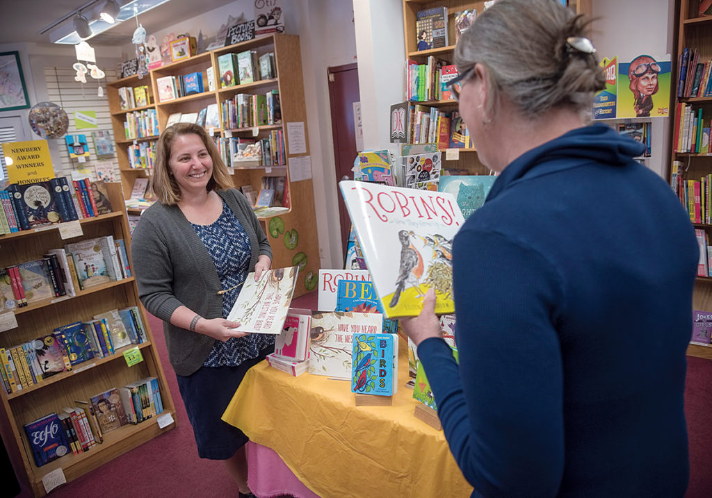 INDEPENDENT OWNER: Jennifer Kandarian, left, store manager at Books on the Square in Providence, speaks with Robin Gross, children’s book buyer. Top left, Kandarian arranges books for display. / PBN PHOTO/MICHAEL SALERNO