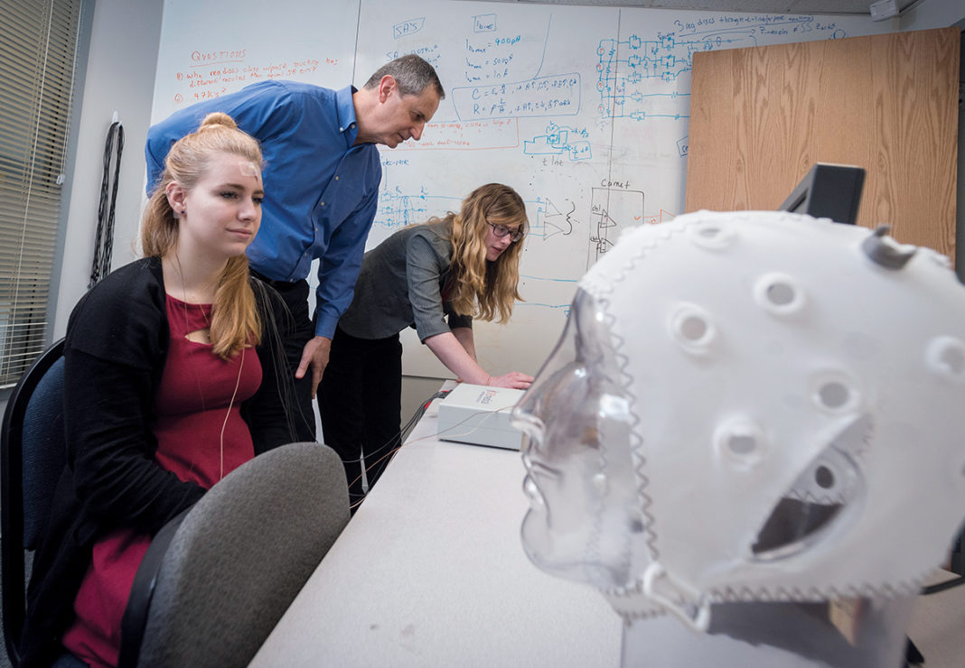 URI STAR: Walt Besio, professor of biomedical engineering at the University of Rhode Island and owner of CREmedical, secured $6 million in a National Science Foundation grant in 2015, a year after he earned two patents for a biomedical electrode that measures brain activity and can be used to potentially stop life-threatening seizures. From left, Jessika Decker, test subject and intern at CREmedical, Besio and Rachel Bartels, product manager at CREmedical. / PBN PHOTO/MICHAEL SALERNO
URI STAR: Walt Besio, professor of biomedical engineering at the University of Rhode Island and owner of CREmedical, secured $6 million in a National Science Foundation grant in 2015, a year after he earned two patents for a biomedical electrode that measures brain activity and can be used to potentially stop life-threatening seizures. From left, Jessika Decker, test subject and intern at CREmedical, Besio and Rachel Bartels, product manager at CREmedical. / PBN PHOTO/MICHAEL SALERNO