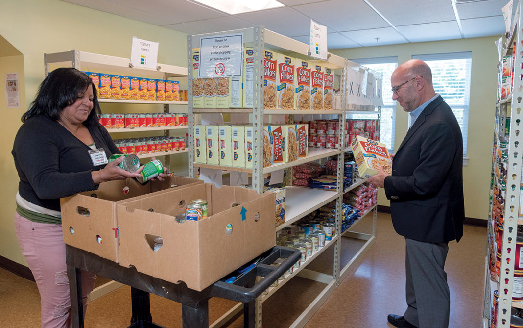 INCREASED RELIANCE: Rhode Island Community Food Bank CEO Andrew Schiff helps volunteer Yve Capella stock the shelves at The Olneyville Food Center at 261 Manton Ave., in Providence. Schiff says there is an increased reliance on emergency food pantries fed by the food bank in the summer months when free and reduced-priced school-meal services are paused, putting greater strain on low-income families to afford food. / PBN PHOTO/MICHAEL SALERNO