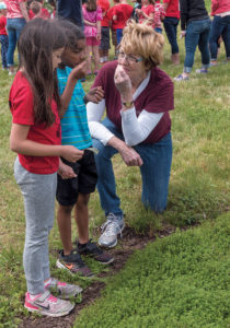 FRESH HERBS: Community School first-graders Emma Rasomgath, 6, left, and Daniel Dubon, 7, smell fresh-cut mint leaves during a visit to the Historic Metcalf-Franklin Farm in Cumberland while Pamela Thurlow, Historic Metcalf-Franklin Farm Preservation Association president, gives a talk about herbs grown on the farm. / PBN PHOTO/MICHAEL SALERNO