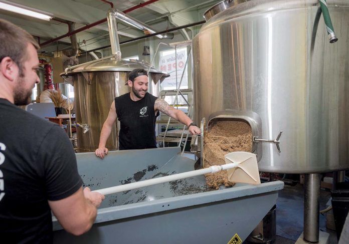 BREWING PROCESS: Co-owners Wes Staschke, left, and Josh Dunlap, take the spent grain out of the mash tun during the process of brewing a batch of ale at Whalers Brewing Co. in South Kingstown. / PBN PHOTO/MICHAEL SALERNO BREWING PROCESS: Co-owners Wes Staschke, left, and Josh Dunlap, take the spent grain out of the mash tun during the process of brewing a batch of ale at Whalers Brewing Co. in South Kingstown. / PBN PHOTO/MICHAEL SALERNO