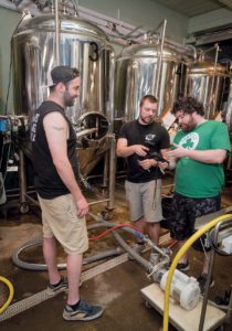 CLEAN TANKS: From left, Josh Dunlap, co-owner of Whalers Brewing Co. in South Kingstown, looks on as co-owner Wes Staschke and brewer Chris Smith use an ATP tester to make sure the fermenting tanks are clean. / PBN PHOTO/MICHAEL SALERNO