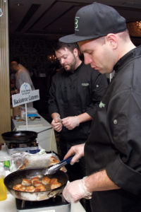 NEWPORT FLAVOR: Patrick Dougherty, foreground, and Tim Horan show what Blackstone Caterers has to offer during last year’s Taste of Newport. / COURTESY KIM FULLER PHOTOGRAPHY