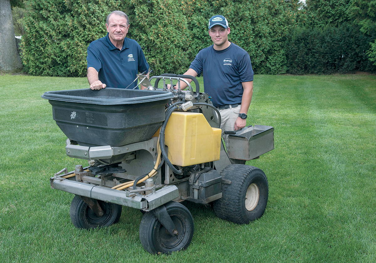 FIRST APPRENTICESHIP: Coventry-based SeaScape Lawn Care Inc. was chosen by the R.I. Nursery and Landscaping ­Association to host the industry’s first apprenticeship program. From left, James Wilkinson, president, and Michael ­Graeminger, senior lawn technician, with their motorized fertilizer spreader. / PBN PHOTO/MICHAEL SALERNO