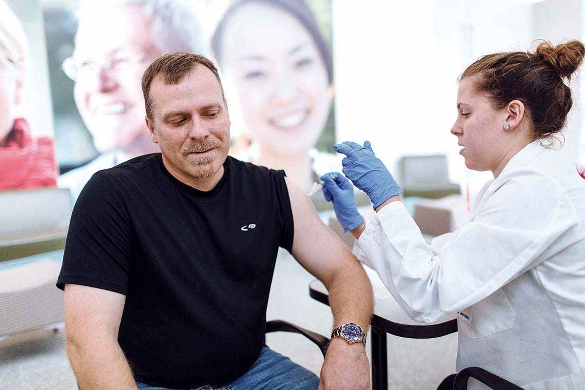 COMPANY PRIORITY: Jeff Guilbert, product-quality leader at Amgen Rhode Island in West Greenwich, receives a flu shot from University of Rhode Island pharmacy student Kate Syder during one of the company’s in-office clinics this past fall. / PBN PHOTO/­RUPERT ­WHITELEY
