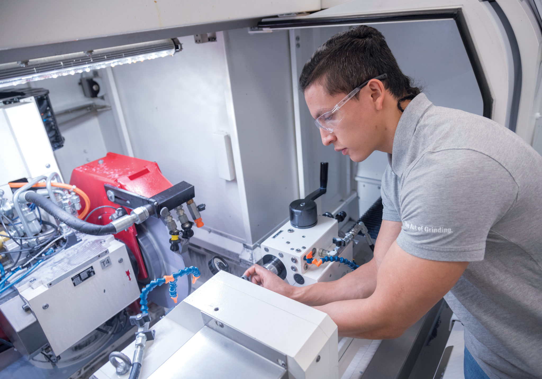 MEASURING UP: Otto Fernandez, a worker at Mahr Federal Inc. in Providence for the past 18 months, and a student in the Shipbuilding/Marine and Advanced Manufacturing Institute machinist program at New England Institute of Technology, takes measurements on a grinding machine. / PBN PHOTO/­MICHAEL SALERNO