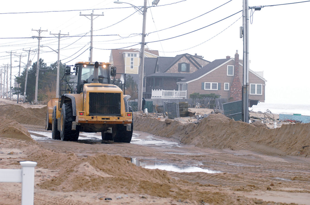DIGGING OUT: A truck clears sand off Atlantic Avenue in the Misquamicut community of Westerly following “Superstorm” Sandy in 2012. Today the town is still dredging 20,000 cubic yards of sand from Winnapaug Pond deposited there during the storm. / PBN FILE PHOTO/BRIAN MCDONALD DIGGING OUT: A truck clears sand off Atlantic Avenue in the Misquamicut community of Westerly following “Superstorm” Sandy in 2012. Today the town is still dredging 20,000 cubic yards of sand from Winnapaug Pond deposited there during the storm. / PBN FILE PHOTO/BRIAN MCDONALD
