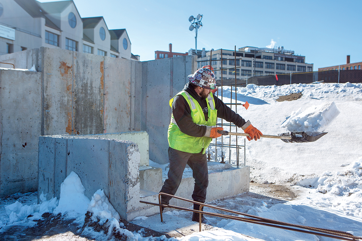 SNOW REMOVAL: A Shawmut Construction worker shovels snow from the work site at 225 Dyer St. in Providence. Construction crews must deal with the winter elements to meet project deadlines. / PBN PHOTO/­ RUPERT WHITELEY