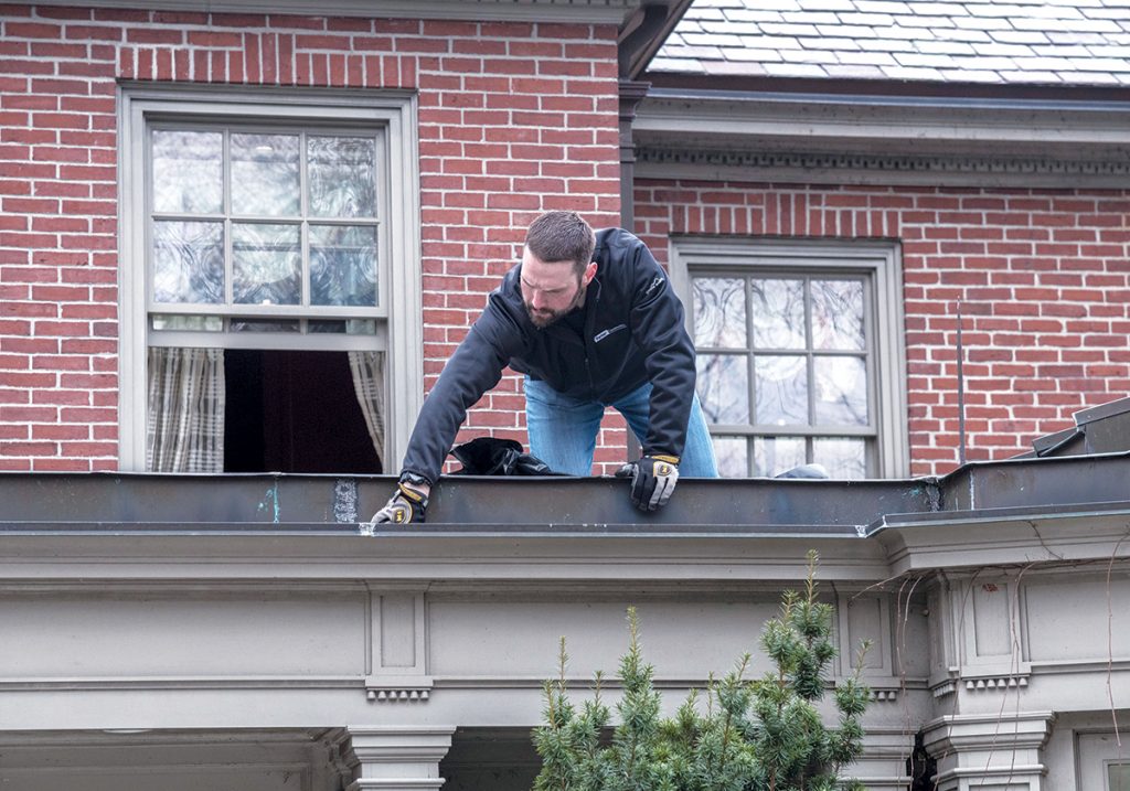CLEANING UP: Brady Parker, director of client services for Parker Construction, cleans gutters on one of the residences the company maintains in Rhode Island. / PBN PHOTO/MICHAEL SALERNO