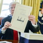 PRESIDENT DONALD TRUMP holds up the tax overhaul legislation after signing it on Dec. 22, 2017. JPMorgan Chase analysts estimate that stock repurchases will hit a record $800 billion this year, much of it financed by the tax overhaul. / BLOOMBERG NEWS FILE PHOTO