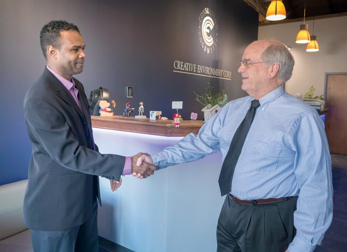 FIRST CLIENT: Evanisio Oliveira, left, owner of Universal Cleaning LLC, shakes hands with Thomas Lent, president and CEO of Thielsch Engineering, which owns Creative Environment Corp. Lent was Oliveira’s first client when he started his cleaning business. / PBN PHOTO/MICHAEL SALERNO