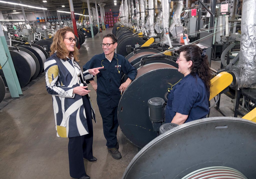 RISE UP: Hope Global in Cumberland was flooded once in 2005 and again during the March 2010 floods. The company has spent upward of $1 million since on flood mitigation. Chief of Staff Leslie Taito, left, with maintenance workers Hector Valentin and Maria Fulns. All the motors of these wire knitter machines were raised about 3 feet. Fulns is standing next to the motor. / PBN PHOTO/MICHAEL SALERNO