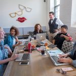 BUILDING BRANDS: David Gomez, standing, co-owner of the Red DWG Library co-working space in Pawtucket, talks with some of the users of the space. From left, seated, are: Natalie O’Sullivan, comedian; The Branding Edit co-founders: Olivia Rodrigues, Patsy Culp and Brittany Taylor; and Ashley Holmes, creative collaborator and stylist. / PBN FILE PHOTO/MICHAEL SALERNO