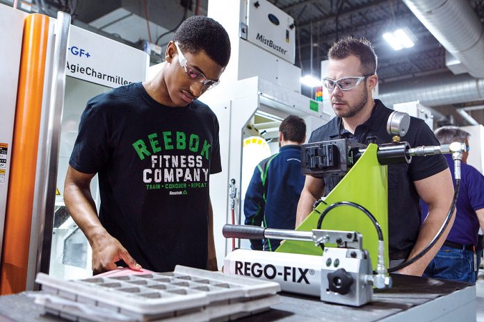 FIRSTHAND: From left, William M. Davies, Jr. Career & Technical High School student Nathanael Chery performs jewelry-machining work at Tiffany, guided by his Machine Technology teacher, Briar Dacier. Chery is part of the school’s work-based learning program. / PBN PHOTO/RUPERT WHITELEY