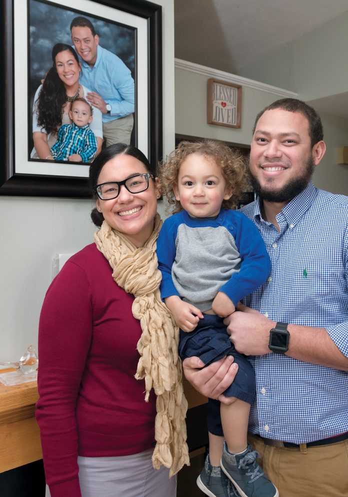 MAKING MEMORIES: Ivette Luna, lead consumer-engagement specialist at Blue Cross & Blue Shield of Rhode Island, with her 2-year-old son Daniel and husband, Jose. The family portrait on the wall was taken during a trip to the Dominican Republic.  / PBN PHOTO/MICHAEL SALERNO