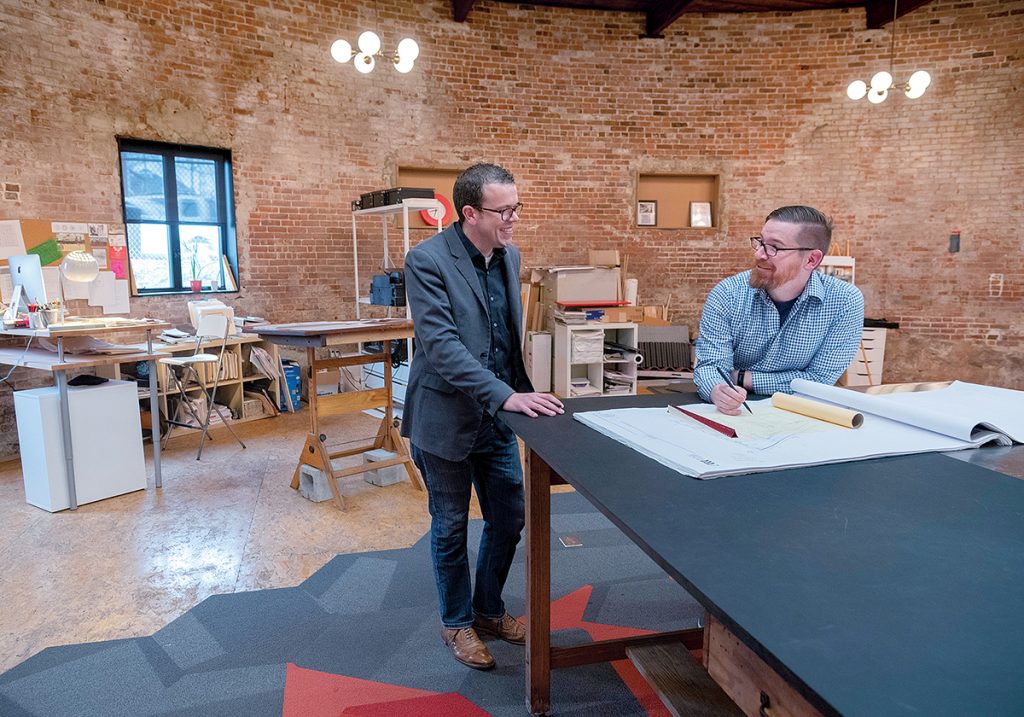 PLANNING: From left, Jay Futrell, project architect, and Eric Army, architect, have a conversation while reviewing plans for a project at Studio MEJA’s rotunda office. / PBN PHOTO/MICHAEL SALERNO