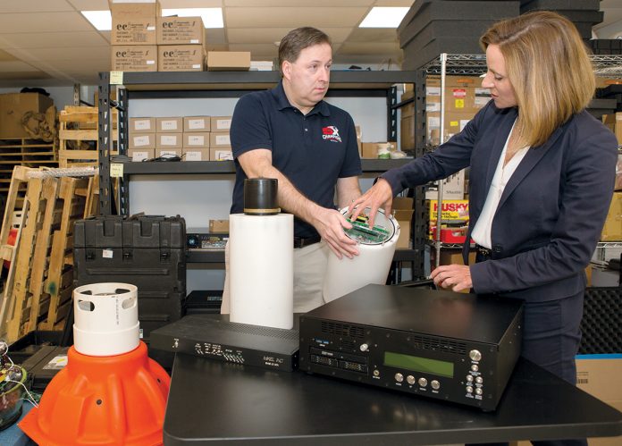 SUBMARINE TECH: MIKEL Inc. President Kelly Mendell speaks with Dave Lambert, engineer and program manager, about the company’s Surface Ship component of its SANS Beacon underwater navigation aid system. The company supports the submarine community with technical and logistic expertise. / PBN PHOTO/KATE WHITNEY LUCEY