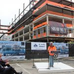 JAMES WOODWARD, superintendent at Shawmut Design and Construction, speaks during the topping off ceremony for the River House apartments project, in which the final steel beam is placed atop the structure. Seated are Commerce Secretary Stefan Pryor, foreground, and Providence Mayor Jorge O. Elorza. / COURTESY SHAWMUT