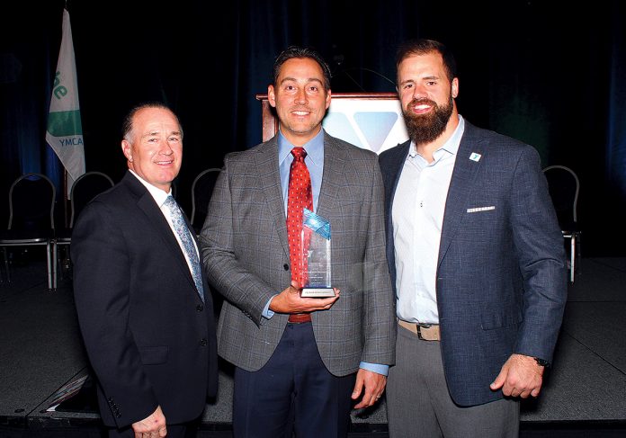STEADFAST SUPPorT: Michael Baker, CEO of Pet Food Experts, accepts an award on behalf of his family from the YMCA of Greater Providence for their longtime service to the Newman YMCA of Seekonk during a Y Heroes Luncheon at the R.I. Convention Center April 12. From left, Greater Providence of YMCA CEO Steven O’Donnell, Baker and New England Patriots fullback James Develin.  / COURTESY PET FOOD EXPERTS