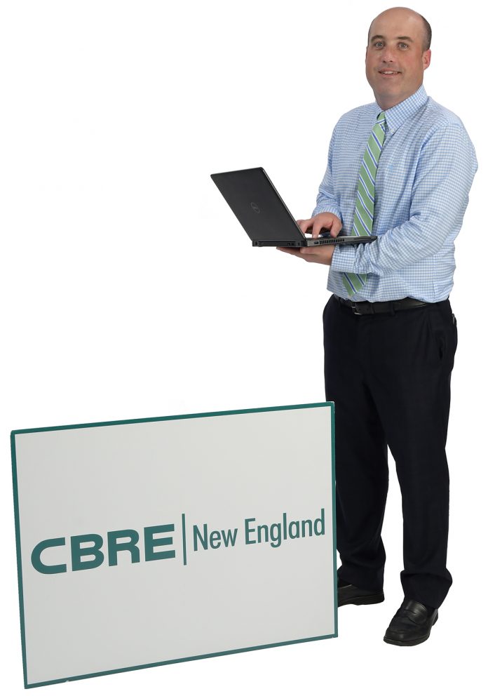 the prop: Andrew Galvin’s laptop and a CBRE sign say it all. “It’s an unbelievable company. … I’m really excited about the future.” / PBN PHOTO/MIKE SKORSKI