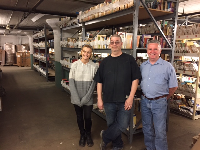 PROACTIVE PHILANTHROPY staff is surrounded by books at its 6-acre, 760,000-square-foot warehouse it shares in New Bedford at 25-51 King St. The bookselling staff includes, from left: Britney Cabral, John Bender and Edward McPherson. / COURTESY PROACTIVE PHILANTHROPY